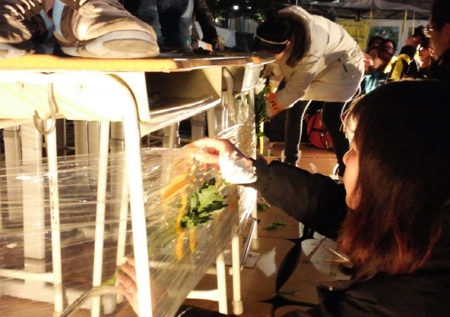 행사 참가자가 비닐로 둘러싼 책상탑에 국화꽃을 꽃고 있다.(사진-고승은)