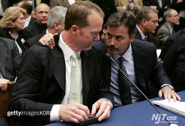 워싱턴 - 3월 17일: 전 세인트루이스 카디널스 선수 마크 맥과이어(왼쪽)가 2005년 3월 17일 워싱턴 DC에서 열린 메이저 리그 야구의 스테로이드 사용 근절 노력을 조사하는 하원 위원회 회의 중에 볼티모어 오리올스의 라파엘 팔메이로와 이야기하고 있다. 맥과이어와 팔메이로는 2007년 12월 13일 전 상원 다수당 원내대표 조지 미첼이 이끄는 위원회가 발표한 미첼 보고서에 이름이 언급되었다. (사진: 마크 윌슨/게티 이미지스)